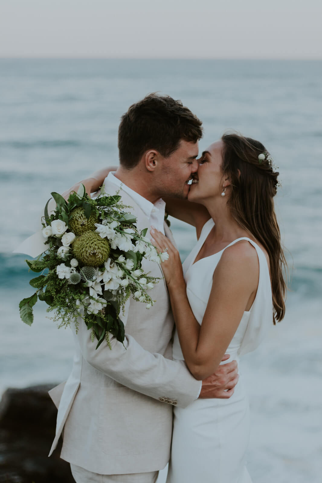 Bride and groom kissing with bouquet in hand.
