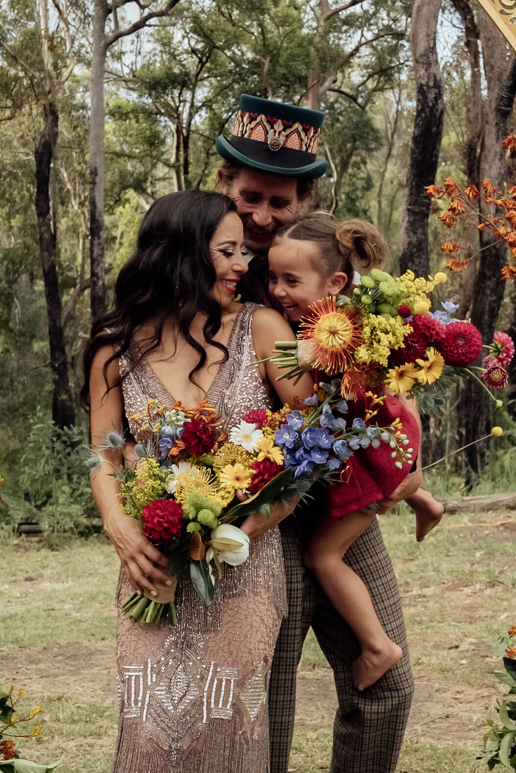 Bride, groom, and child under the wedding arch with flowers.