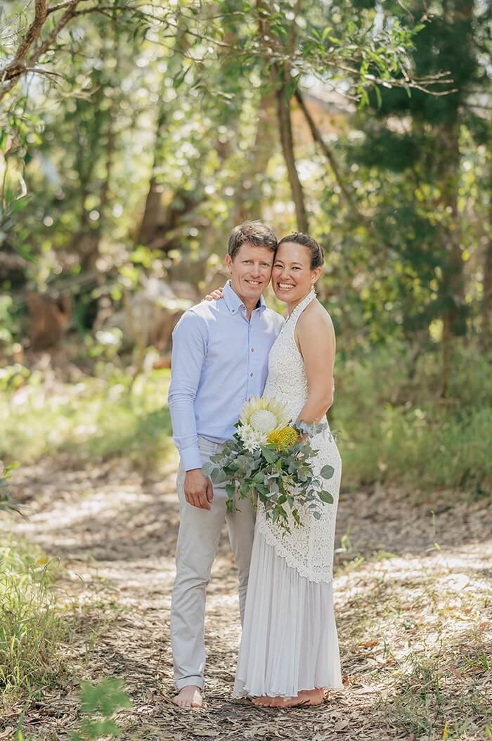 Bride, groom, and child under the wedding arch with flowers.